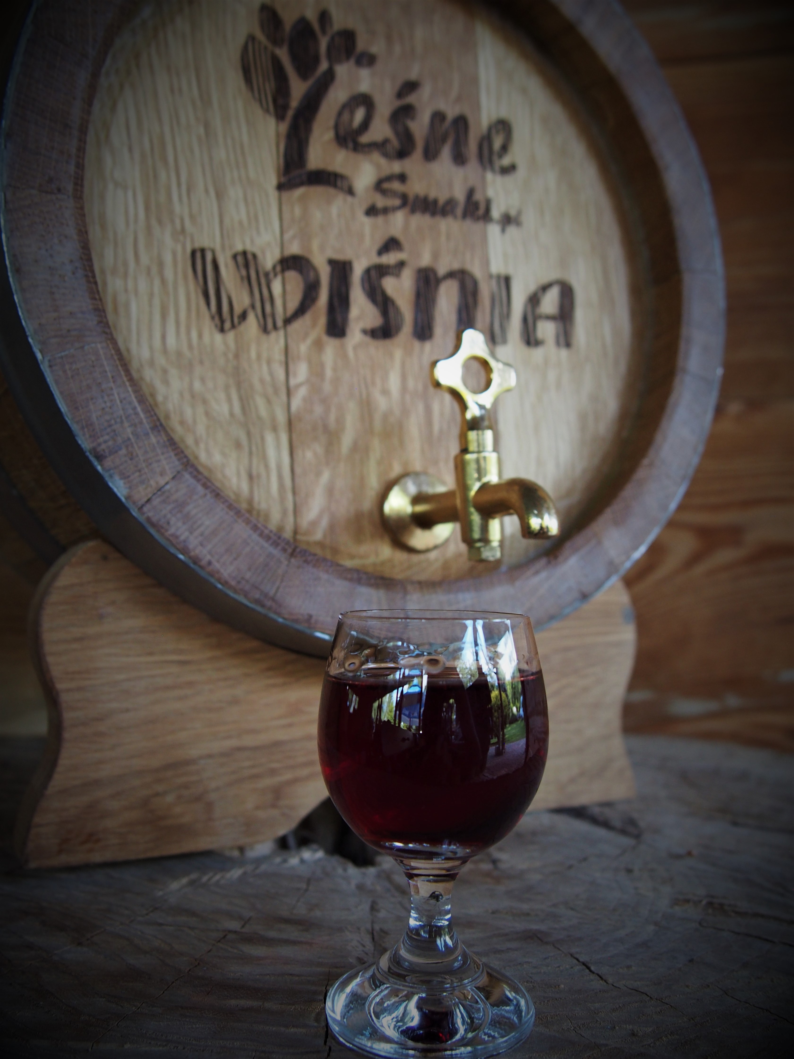 Kieliszek z czerwonym winem, w tle beczka wina, Leśne smaki.